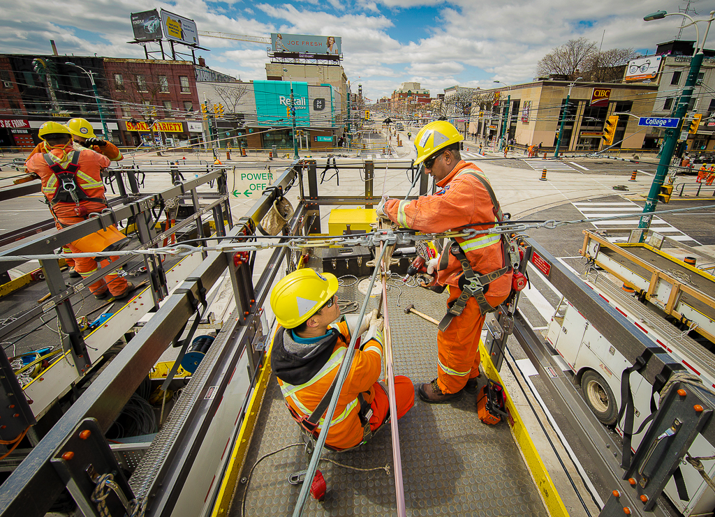 Image of TTC overhead employees working on wires along a busy intersection.
