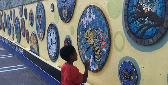 A boy views an artistic mural on a long wal that consists of mosaics.