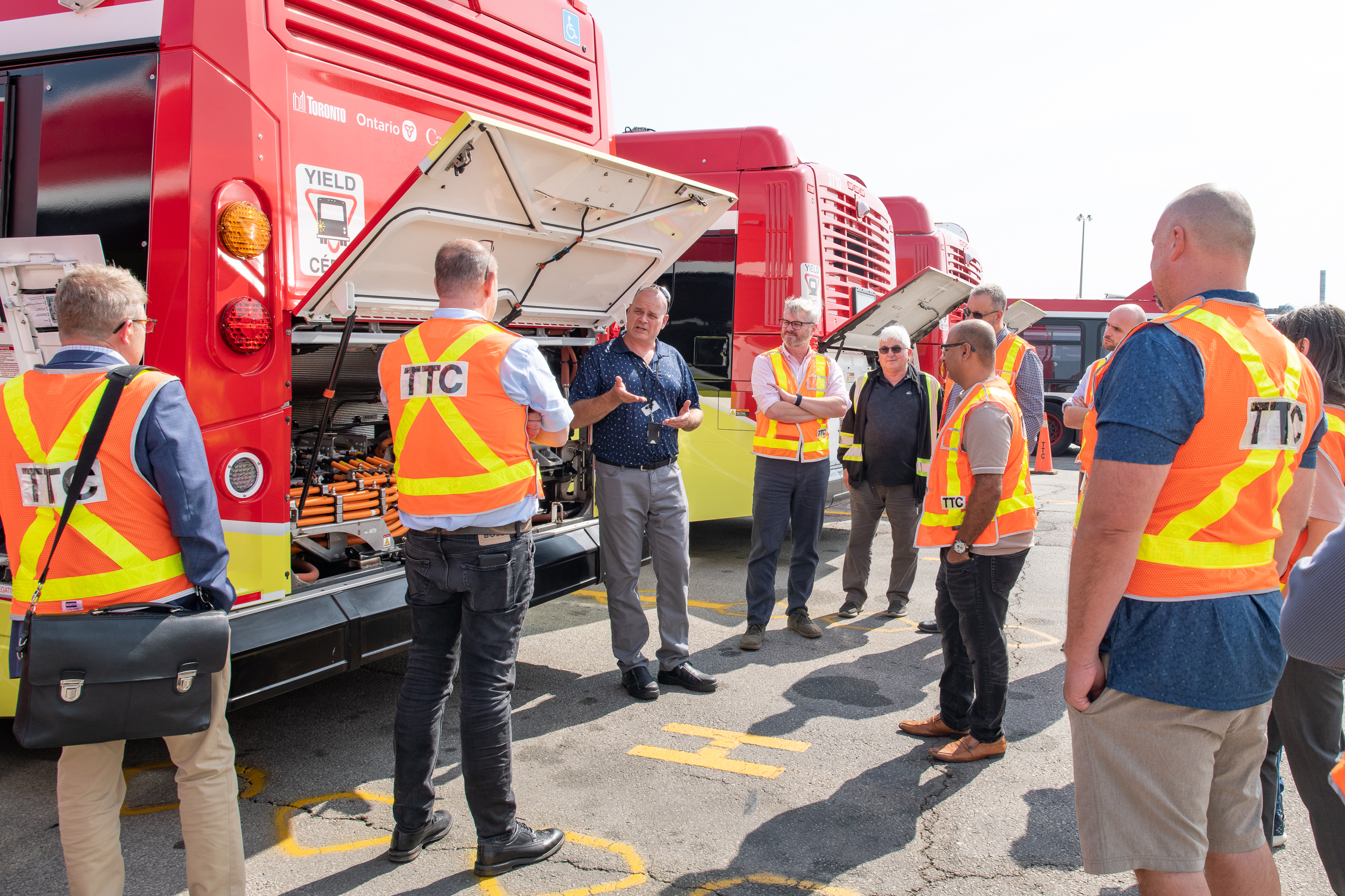 A group of individuals in safety vest listen to the presenter in front of the TTC eBus.