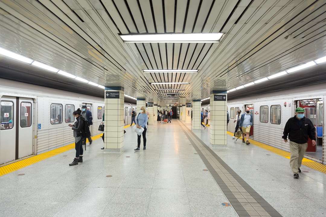 On the platform for Bloor-Yonge Station. Subway trains have arrived on each side of the platform. The left side train is still closed and passengers are waiting to board. The right side train is open and passengers are exiting the train. 