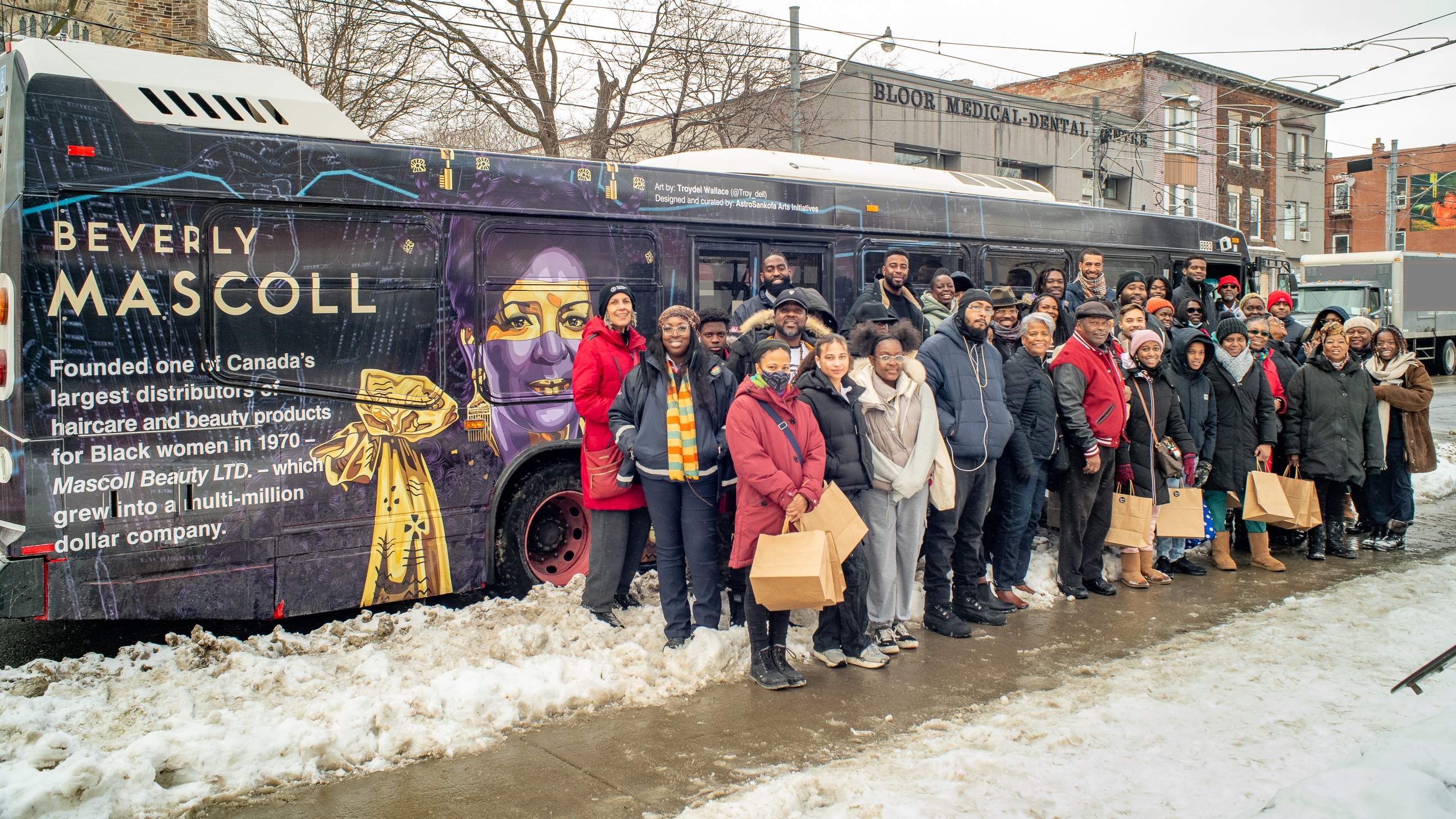 People lined on sidewalk in front of wrapped bus