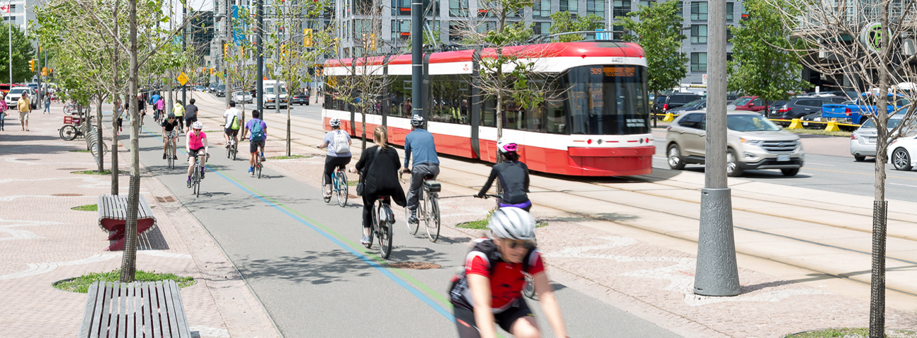 Low-floor streetcar passes in the background with cyclists in the bike lanes in the for ground on Queens Quay