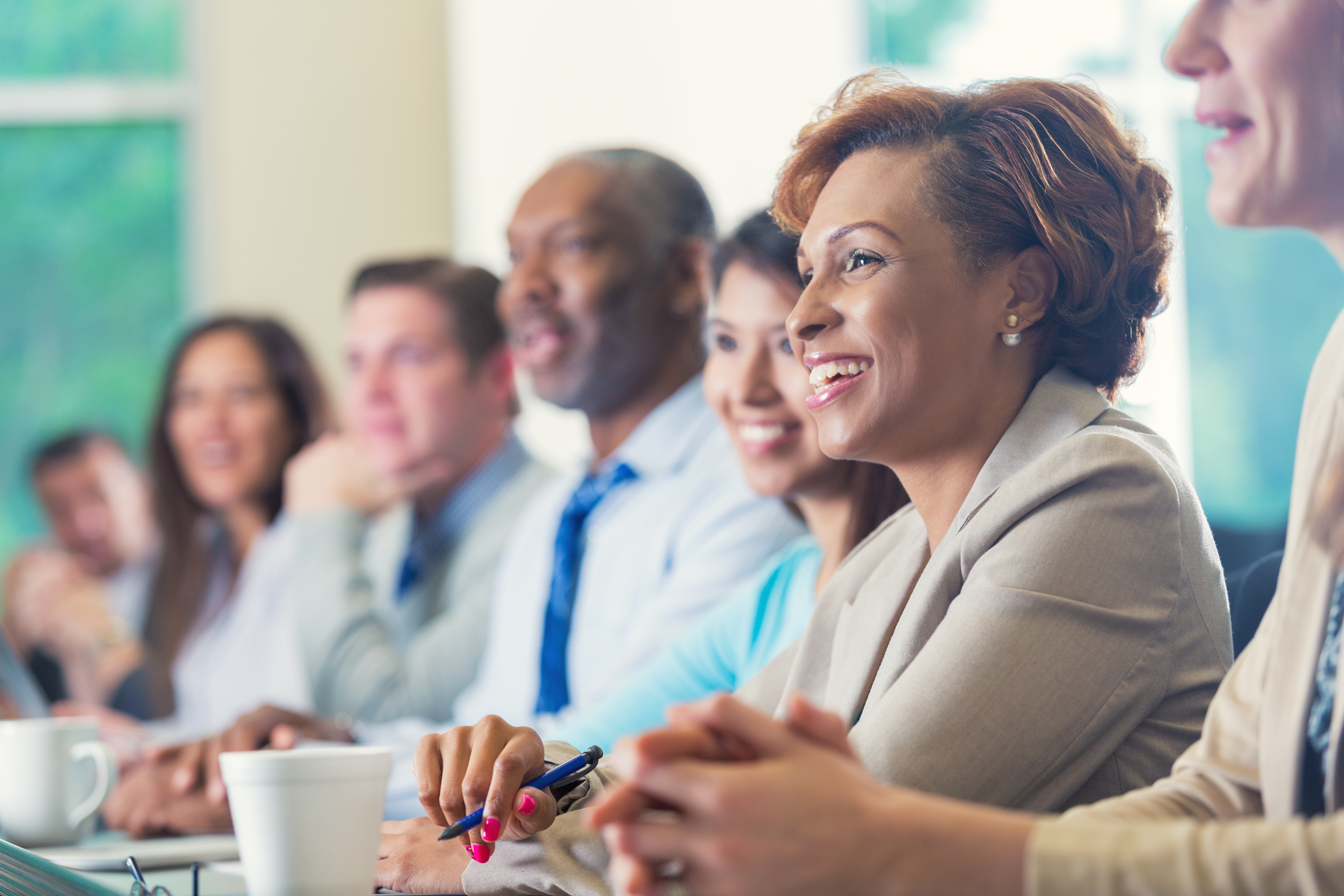 A diverse group of individuals sitting beside each other in a meeting room at work.