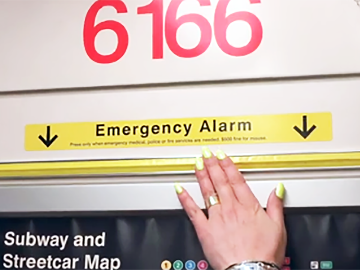 A person's hand pushing the yellow Emergency Alarm onboard a subway train.