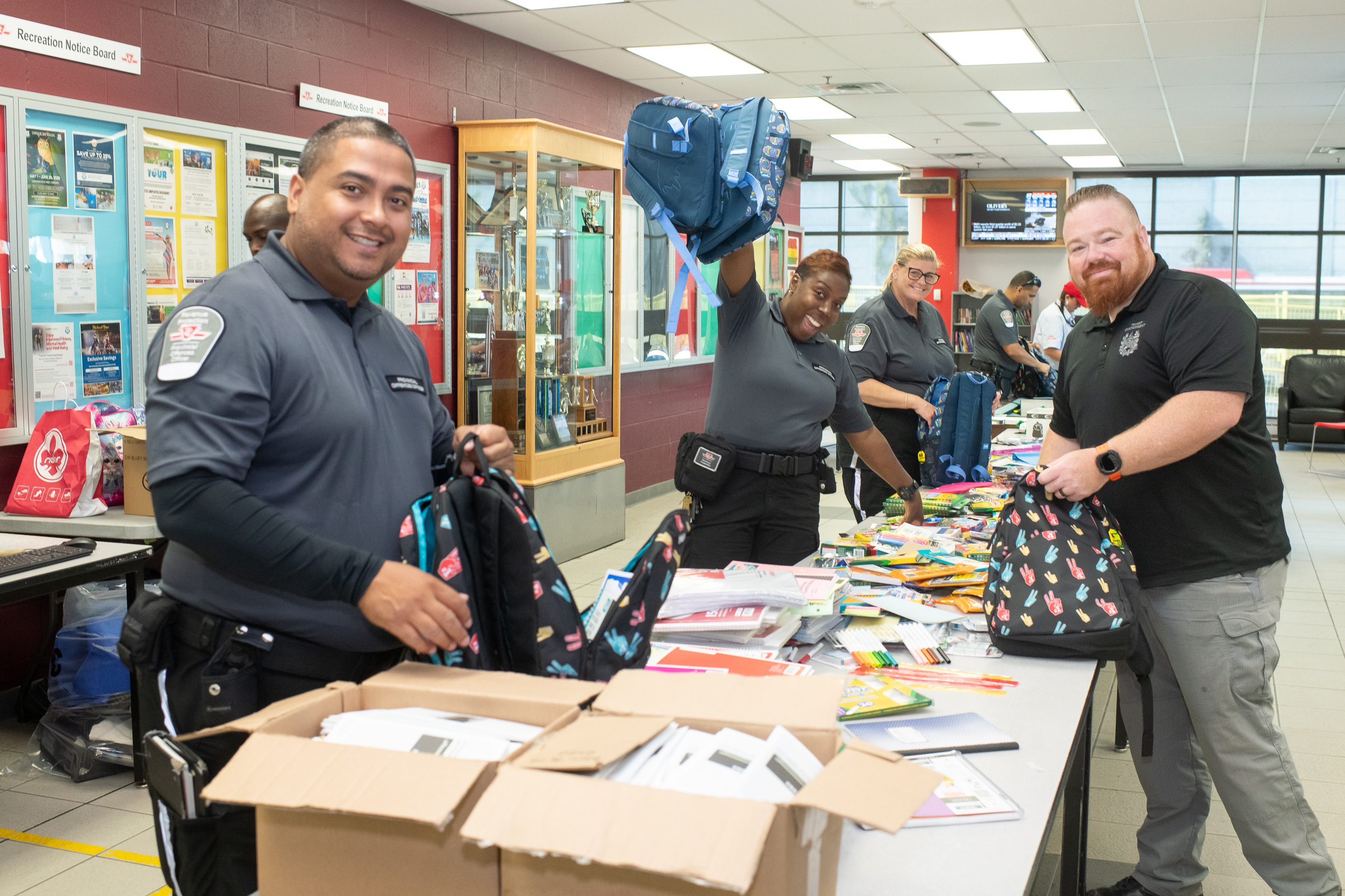Group of TTC staff smile and fill backpacks with essential school supplies.