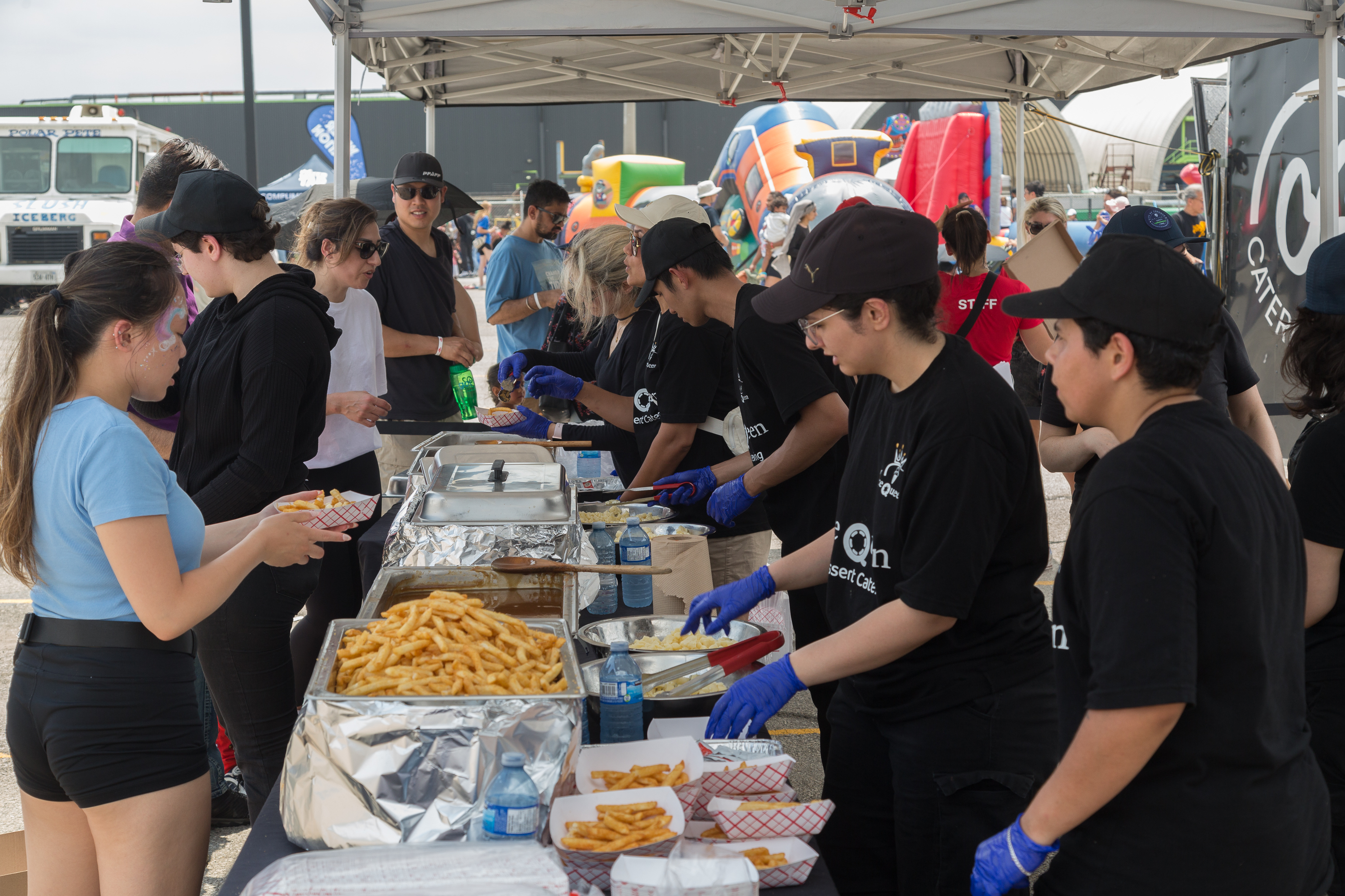 People in matching outfits standing on one side of a table full of food with other people taking food from the table.