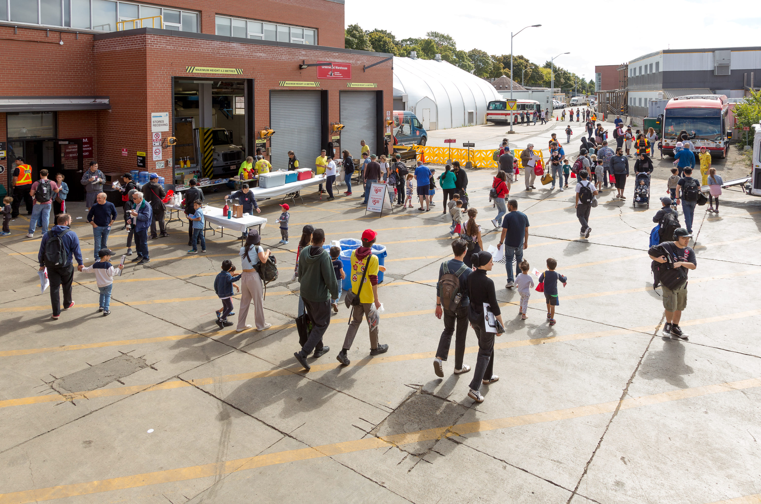 Crowds of families walking through the outdoor lot at the TTC Greenwood Yard Open House, with vehicles, tents, and tables in the background. 