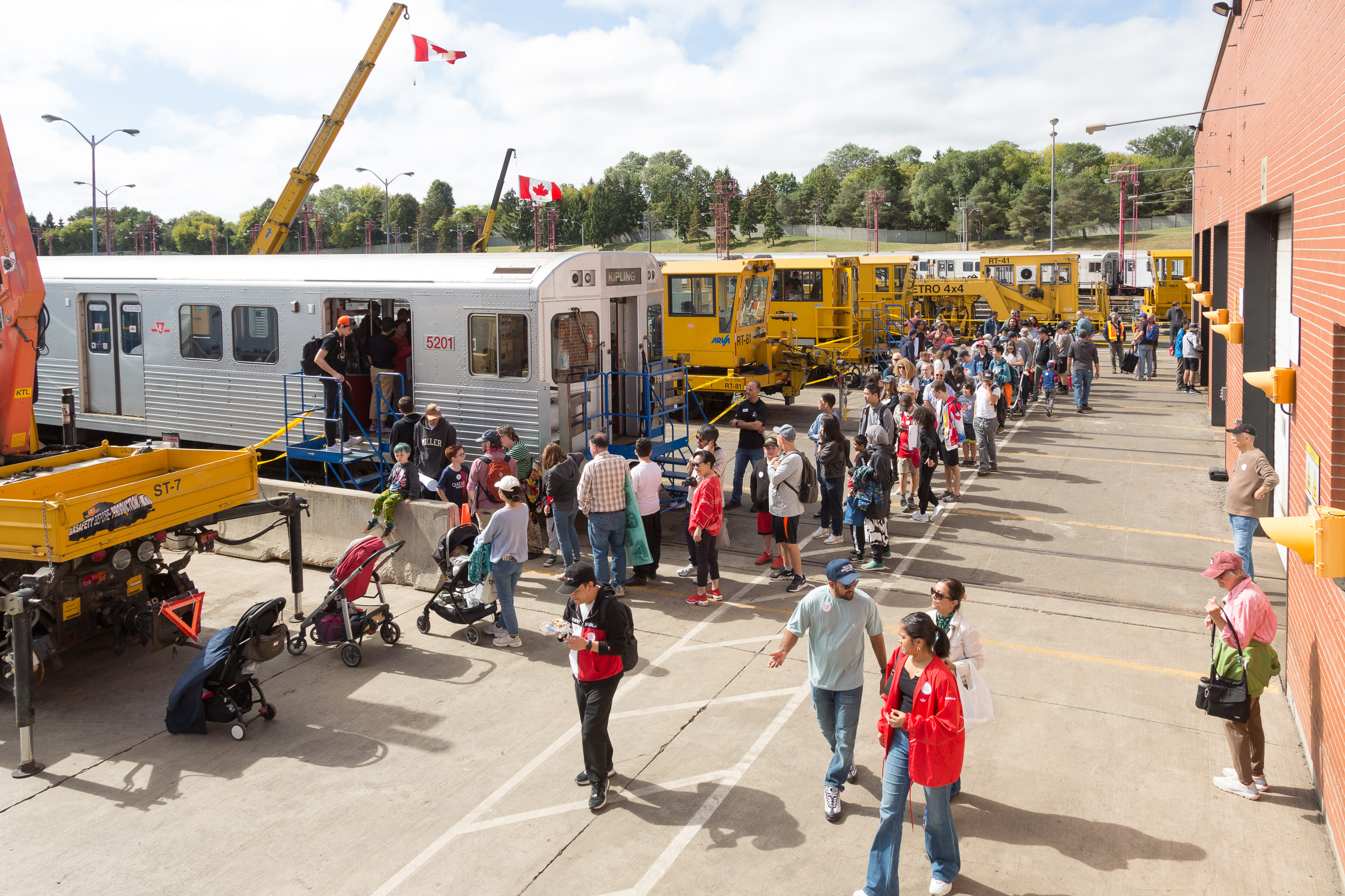 A line of visitors for the Subway Simulator at the Greenwood Yard Open House, with several vehicles in the background. 