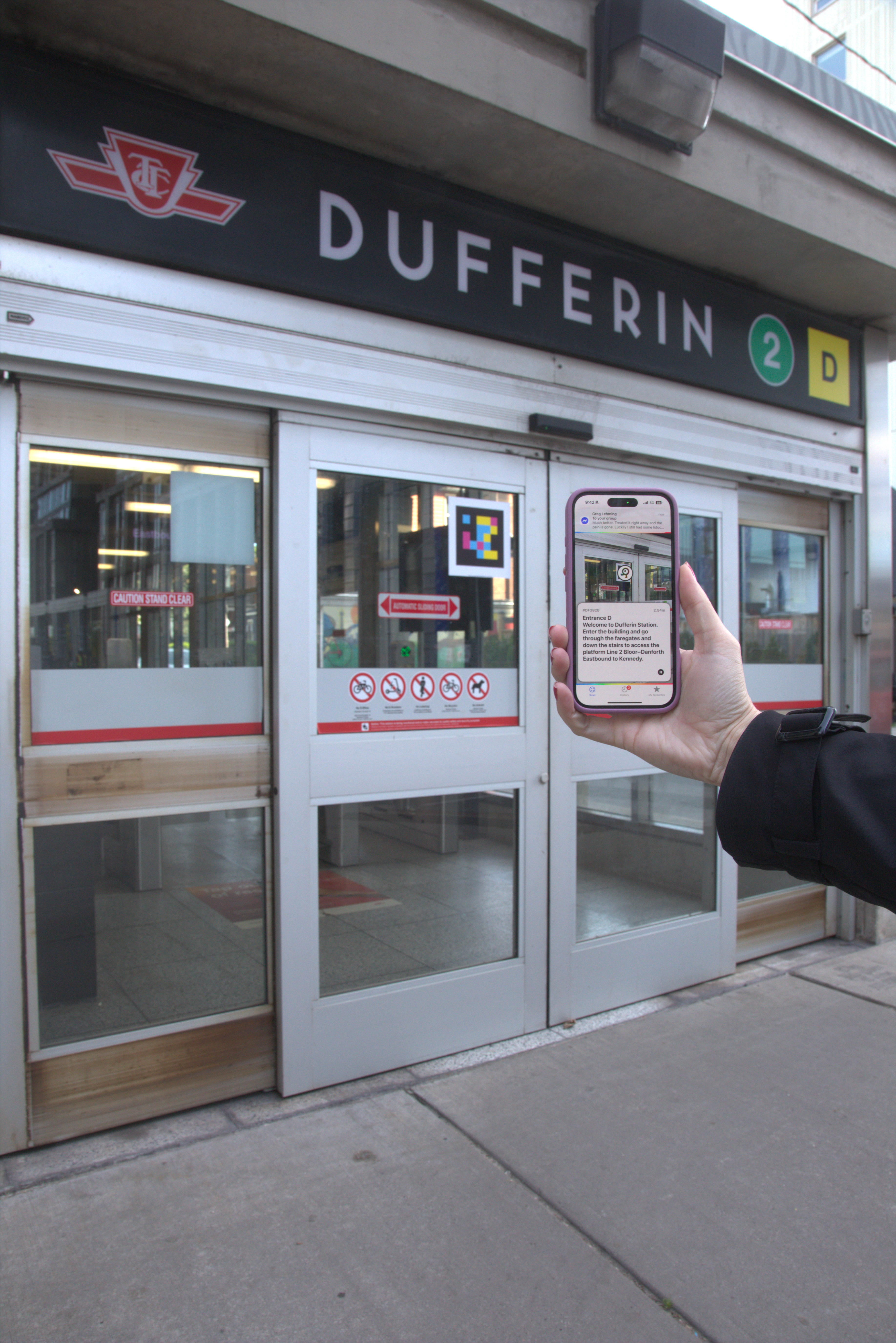 A hand holding a phone that is scanning a NaviLens code at the entrance of Dufferin Station.