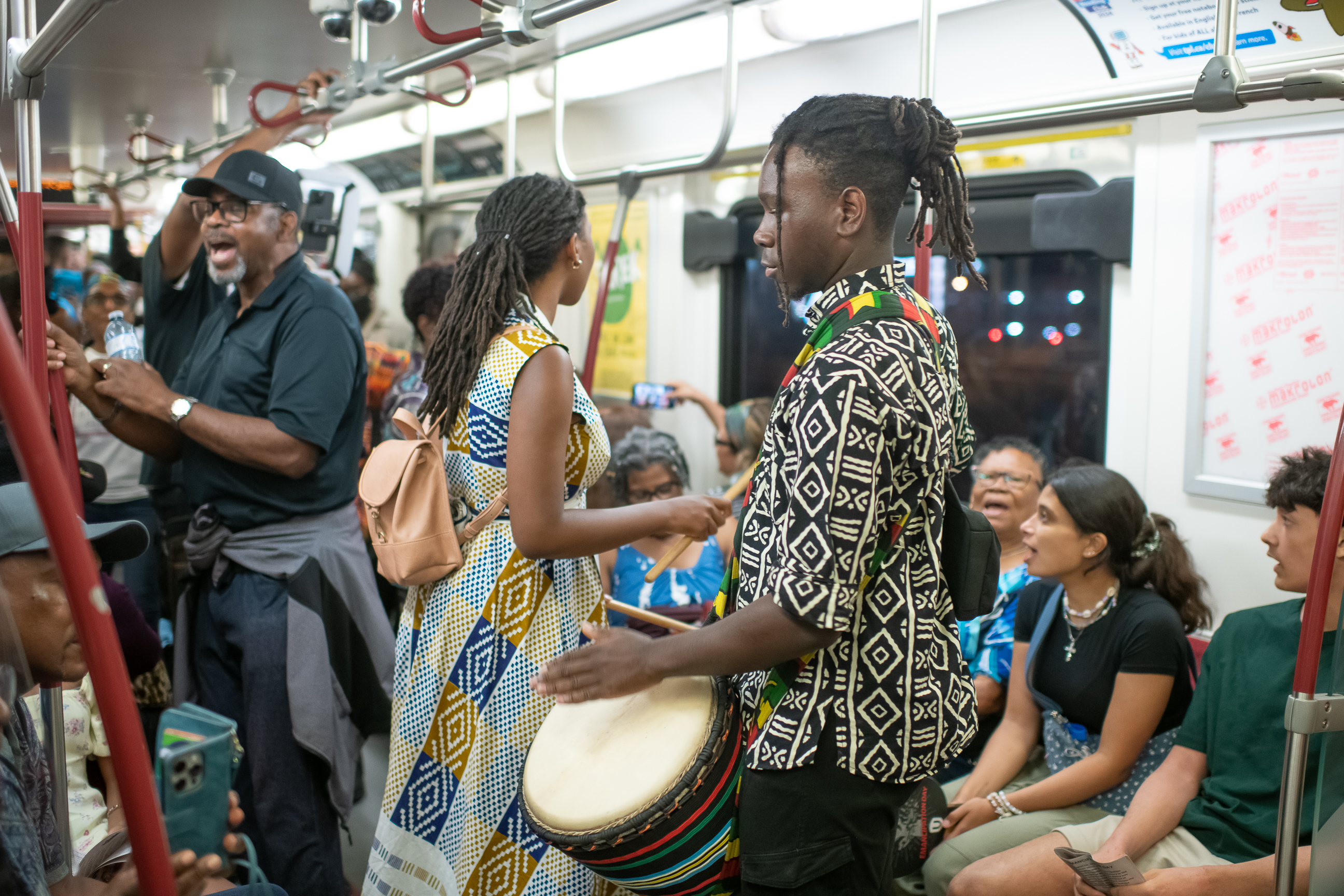 A person playing a drum on the Freedom Train Ride. Various participants are seen singing in the background.