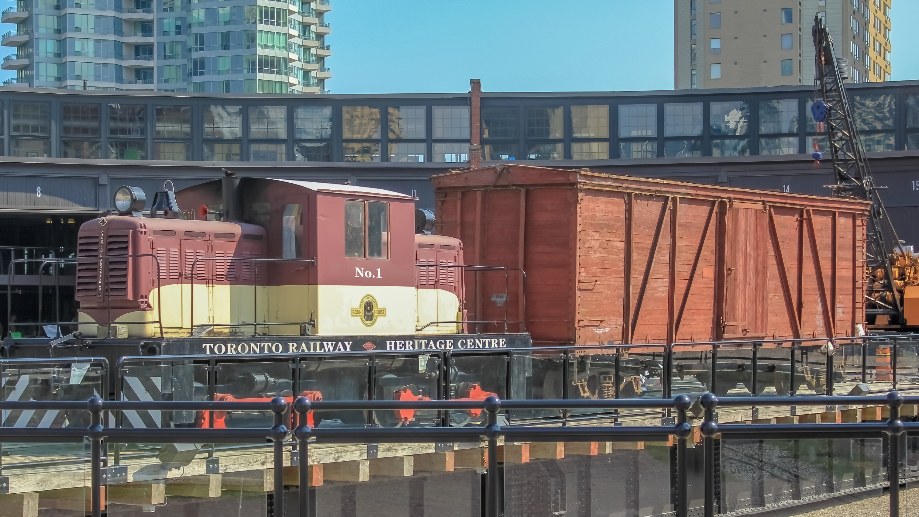 A vintage brown and yellow train in front of a black curved building at the Toronto Railway Heritage Centre.
