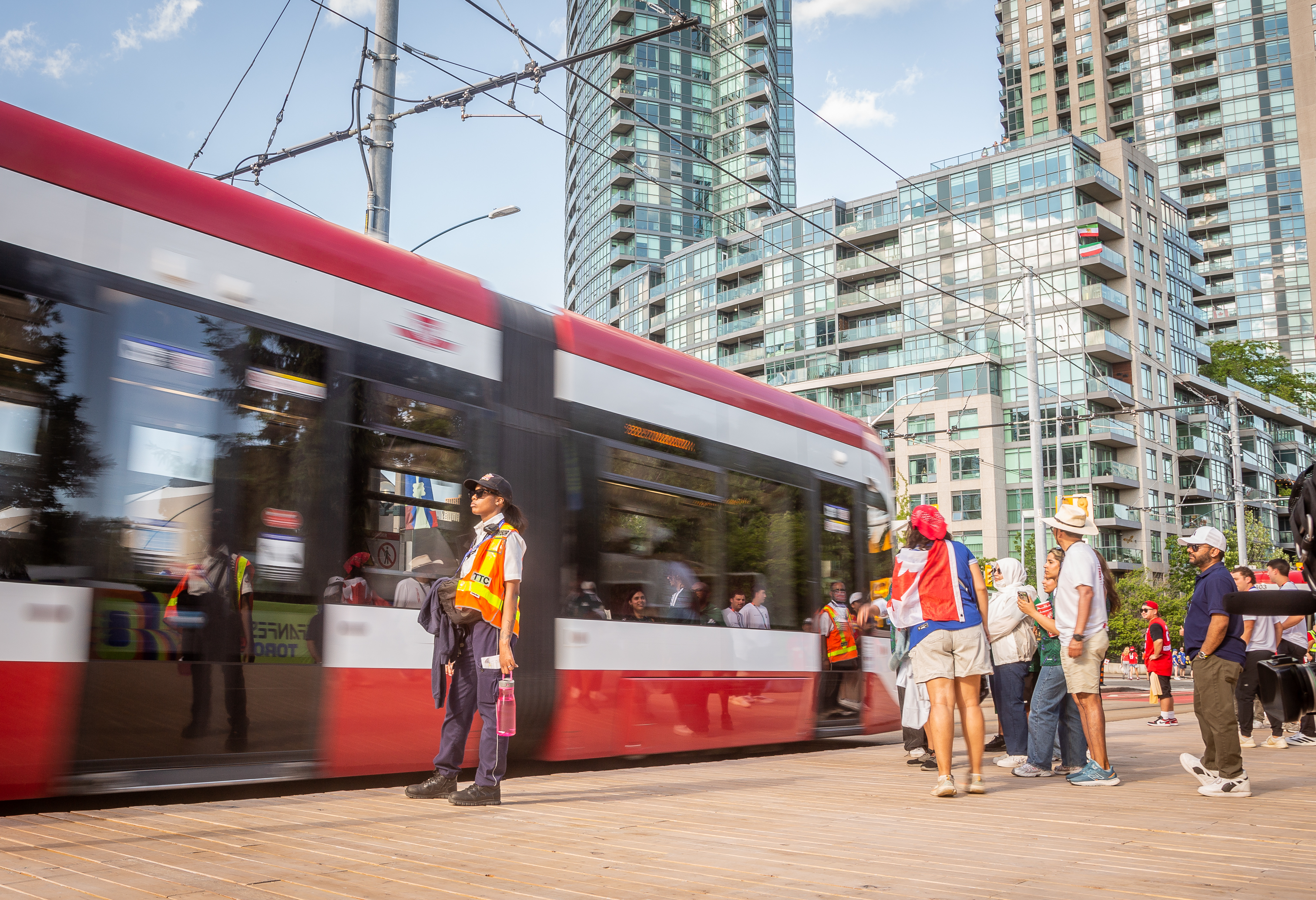 A TTC employee stands on the sidewalk while a crowd prepares to enter a TTC streetcar.