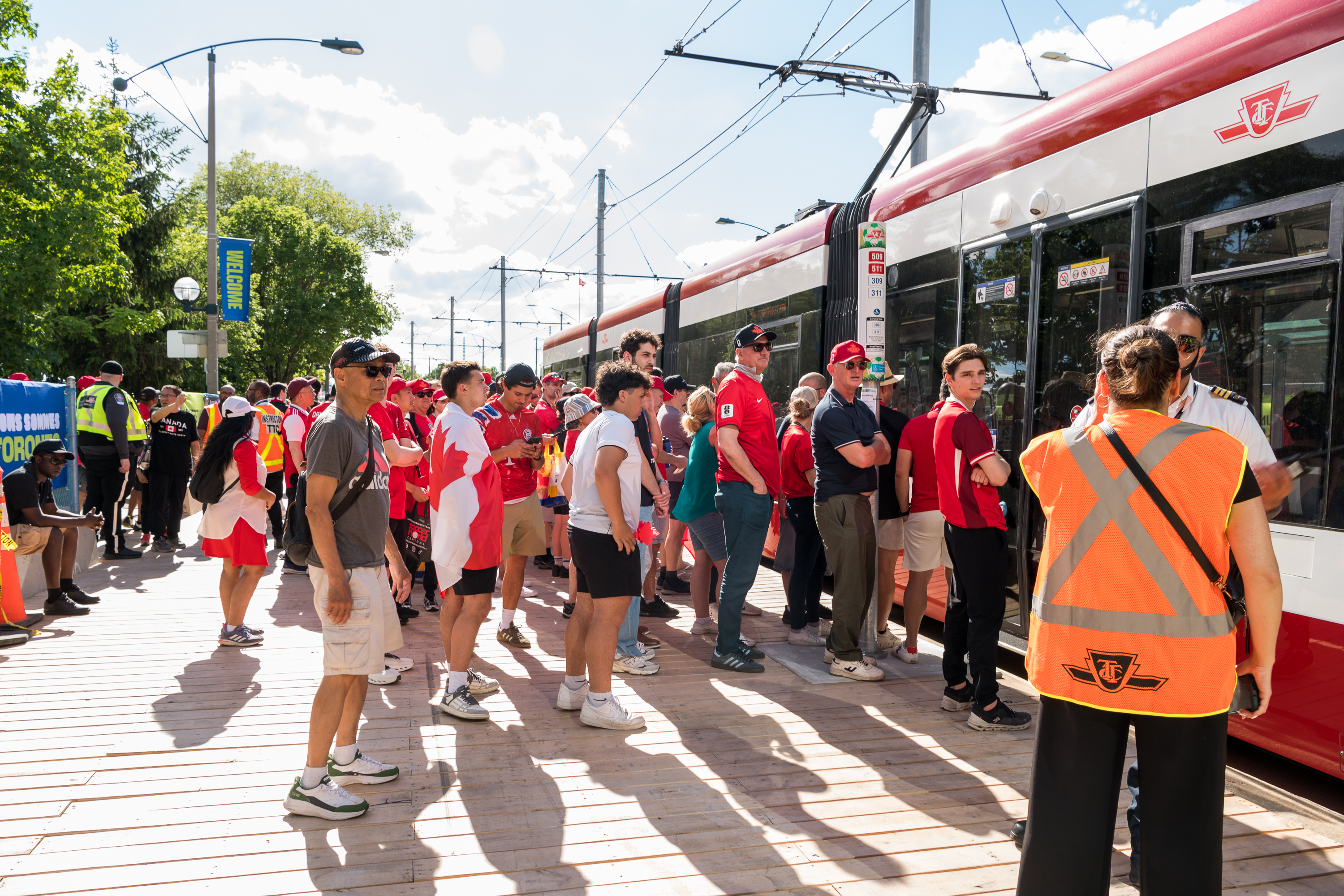 Fans wearing Team Canada clothing and flags boarding a streetcar with two TTC employees nearby. 