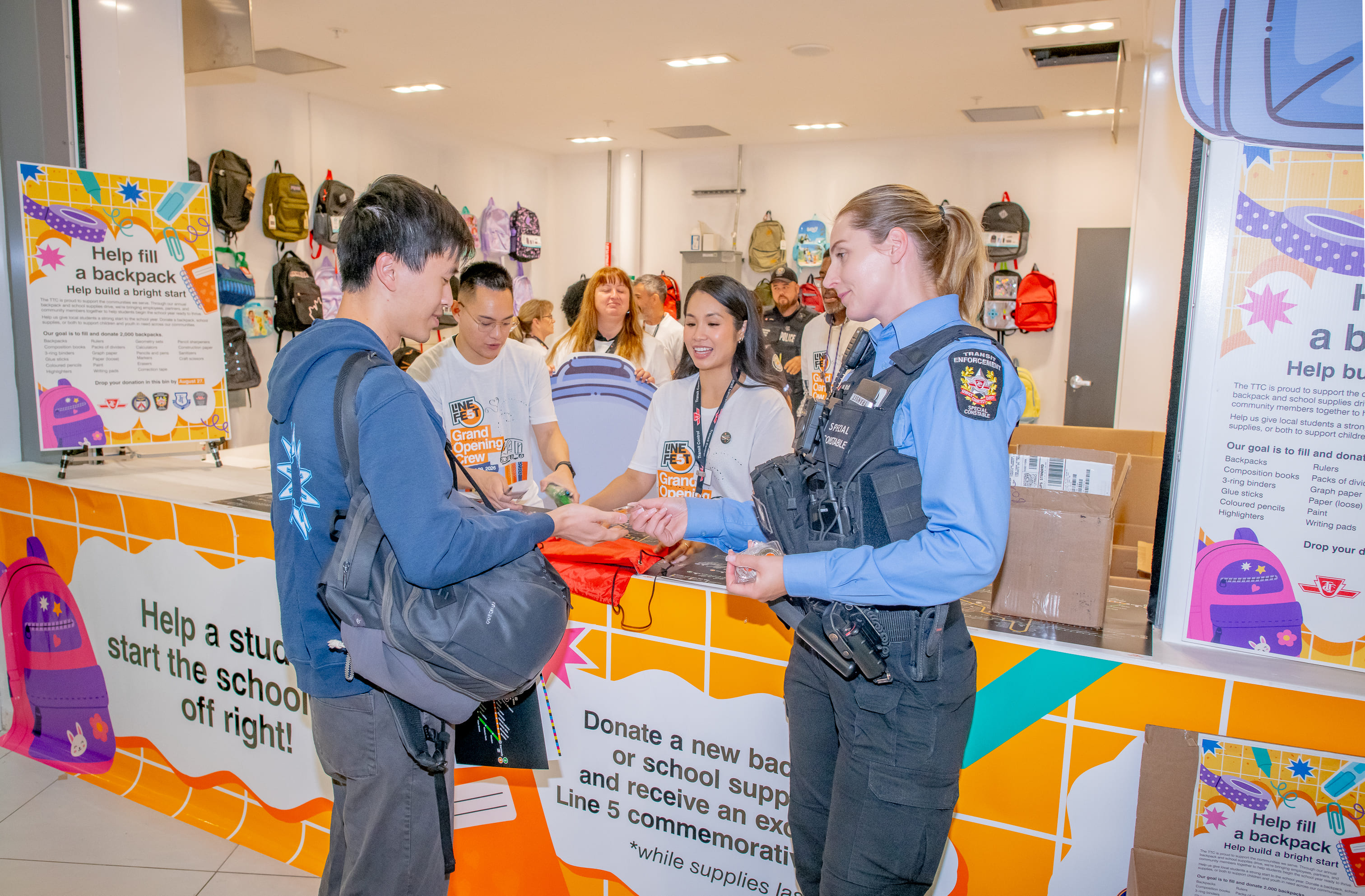 A visitor donating a backpack for the TTC Backpack Drive and being given a limited-edition Line 5 coin, from a special constable.
