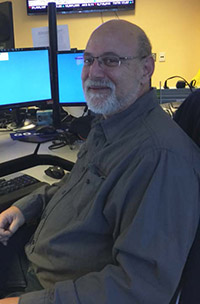 Eric Gottlieb, a Wheel-Trans Dispatcher, sits with smile on his face, with computer and office desk in background