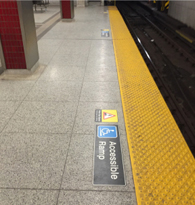 Photo of subway platform floor with a Accessible Ramp decal and a Mind the Gap decal before the yellow safety strip.