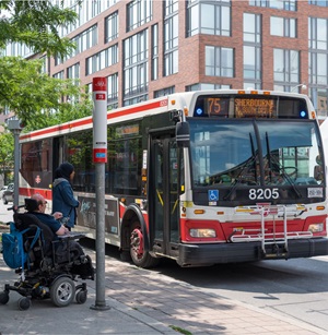 A customer using a motorized wheelchair waits to board a conventional bus