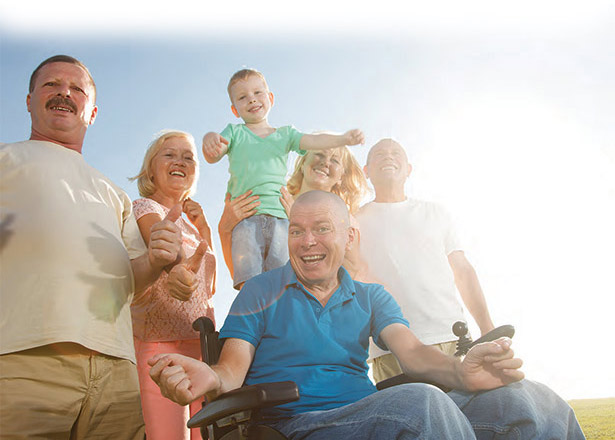 A diverse group of people smiling outside, on a bright and sunny day.