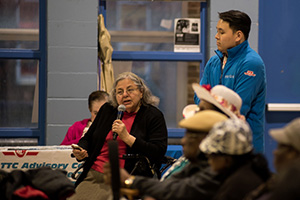 audience speaking into a microphone in meeting while other members listen attentively