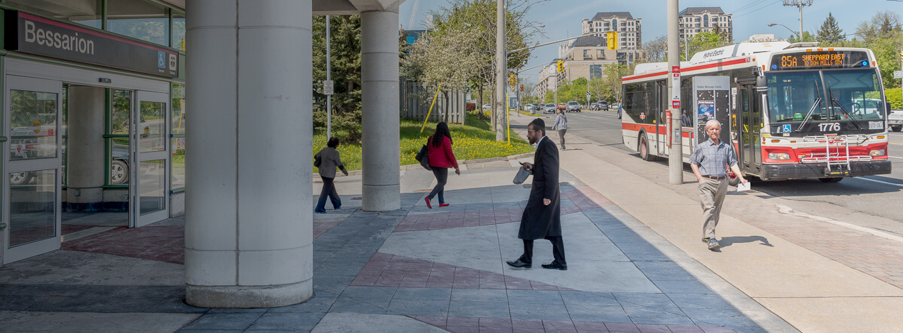 Transit Commuters walking toward waiting Bus near Bus Stop  outside of Bessarion Station Entrance 